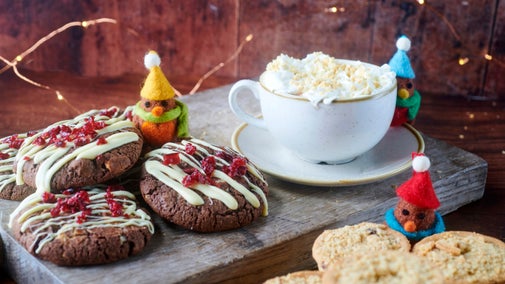 A plate of chocolate biscuits, striped with white chocolate, and a cup of hot chocolate topped with whipped cream